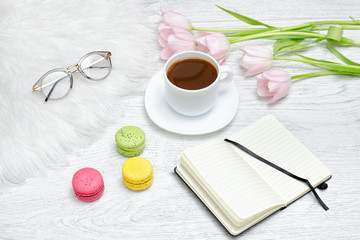 Notepad, tea mug, and pink tulips. Light wooden background.