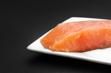 Plate with fillet of red fish on black background.