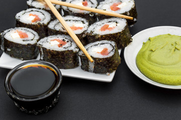 Sushi and chopsticks on the plate with soy sauce and wasabi on a black background.