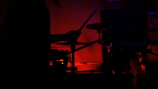 Unrecognizable male drummer silhouette playing the drums. Red light, low key. Entertainment and art concept
