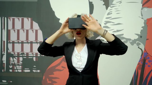Pretty girl is wearing optical head-mounted display. She is walking over corridor groping an air by hands, wondering