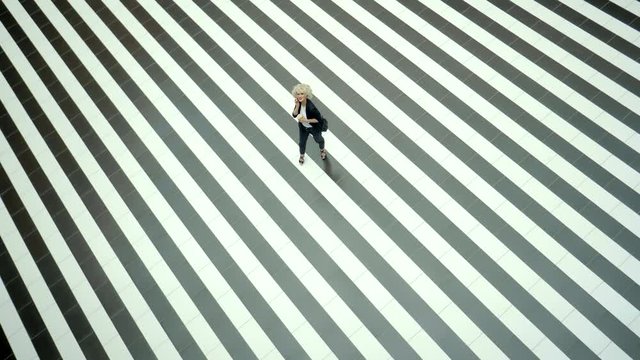 Young fashion woman is posing on an abstract tiled floor with black and white stripes. View from top, she is looking so small