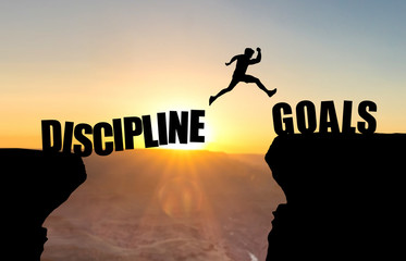 Mann spring über Abgrund vor Sonnenuntergang mit Beschriftung Discipline/Goals.