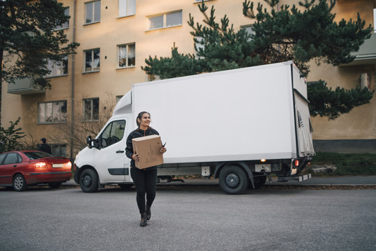 Full length of female worker carrying box while walking against delivery van on street