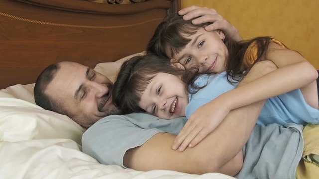 Happy family on the bed. Father hugs his daughters. Daddy's girl.