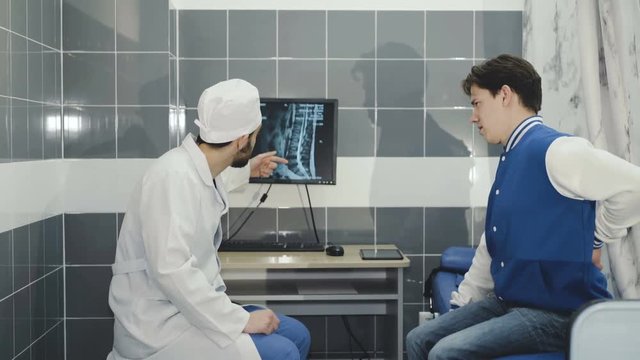 A doctor who examines a patient shows the injured spine on the monitor. 4k