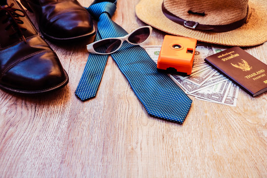 Top view accessories for travel on old wood, Shells, yellow camera ,shoes ,glasses necktie ,  hat ,and Dollar on Thailand passport. photo concept travel and life style. 