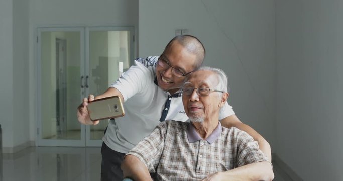 Young man and his elderly father taking selfie photo together with a mobile phone at home. Shot in 4k resolution