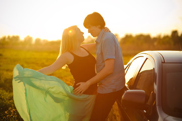 A loving couple watching beautiful bright romantic sunset after journey, standing leaning against...