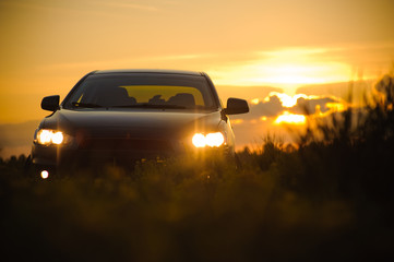 Blue sport car with headlights in a field in bright sunset light at summer evening