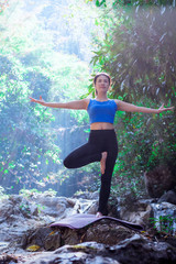 Sporty young woman doing yoga practice with stream and forest background - concept of healthy life and natural balance between body and mental development