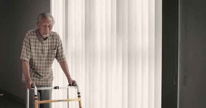 Senior man with grizzled hair, walking near the window while holding a walker. Shot in 4k resolution