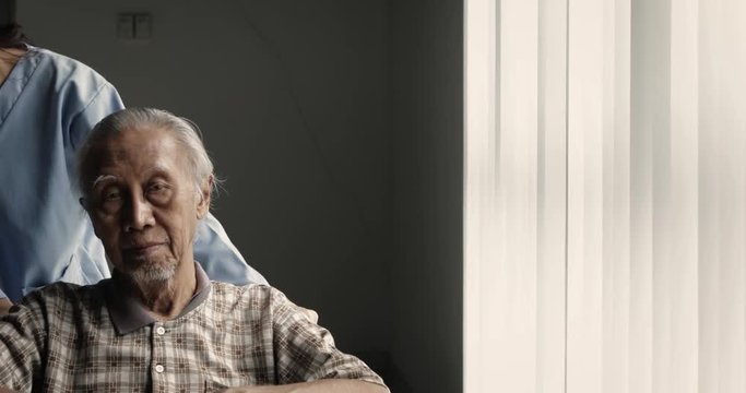 Senior Asian man sitting on wheelchair and pushed by his nurse near the window in hospital. Shot in 4k resolution