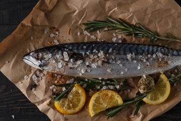 Raw mackerel with lemon, herbs and spices on a dark wooden table.
