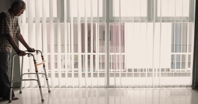 Full length of an elderly man walking near the window with a walker in the hospital. Shot in 4k resolution