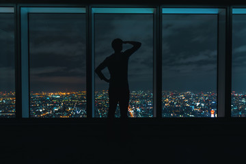 Man looking out large windows high above a sprawling city at night