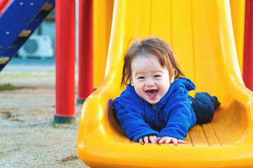 Fototapeta na wymiar Happy toddler boy playing on a slide at a playground