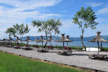 Fototapeta na wymiar Straw umbrellas on the Lake Skadar beach. Albania - Montenegro border.