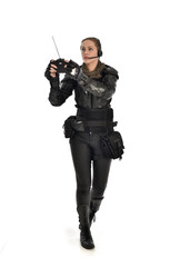 full length portrait of female  soldier wearing black  tactical armour, holding a remote control, isolated on white studio background.