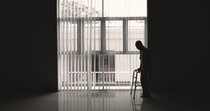 Silhouette of elderly man walking near the window while using a walker. Shot in 4k resolution