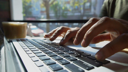 Modern laptop on table. Cup with fragrant coffee stand next laptop. Light from the window falls on working surface. Man types message. Concept of advertising different sites and social networks or