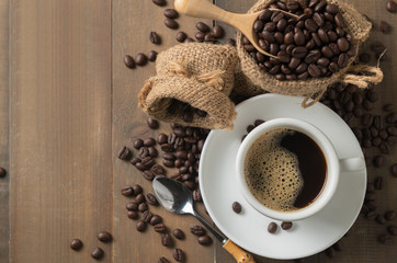 Hot black coffee on cup and roasted coffee beans in wood scoop on old wood background, top view and copy space for text