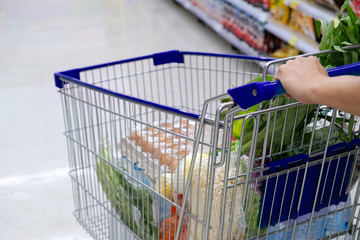 Close-up of woman with shopping cart purchasing food in a supermarket.