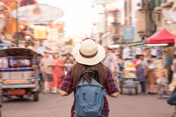 Young Asian woman with hat and backpack traveling in Khaosan Road among people, walking outdoor market in Bangkok, Thailand.