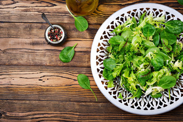 Fototapeta na wymiar Fresh leaves of mix salad in a bowl on a wooden background. Flat lay. Top view