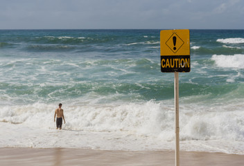 Caution sign due to dangerous surf, with male about to enter the water.