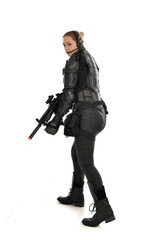 Naklejka premium full length portrait of female soldier wearing black tactical armour, holding a rifle gun, isolated on white studio background.