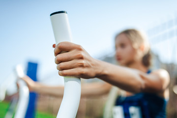 young woman using outdoor gym equipment in in a blue shirt and leggings the park.