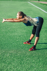 sports girl in a blue shirt and leggings doing gymnastics workout on a football field. Fitness, sport, health energy.