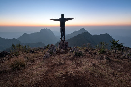 tourist enjoying sunset on top of a mountain, Man stay on the peak of high rocks  and rise his hands up