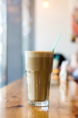 A glass of latte on a wooden table in the cafe. Freshly prepared drink covered with foam. From a glass tube sticking out. Photo is suitable for menu design, advertising and recipe book.