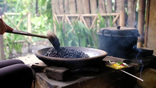 Stirring uncooked coffee beans in frying pan in old traditional way by hand. Stage of preparing true coffee powder