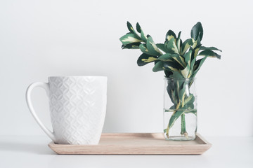 Small glass vase with yellow-green leaves and ceramic mug on bamboo tray