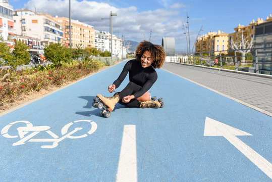 Young smiling black girl sitting on bike line and puts on skates.