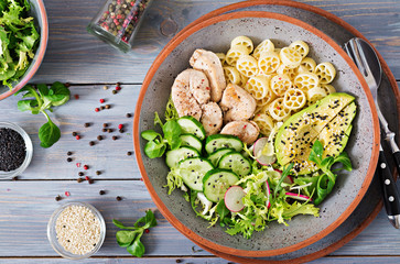 Healthy salad with chicken, avocado, cucumber, lettuce, radish  and pasta on dark background. Proper nutrition. Dietary menu. Dinner. Flat lay. Top view