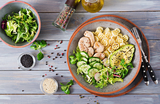 Healthy salad with chicken, avocado, cucumber, lettuce, radish  and pasta on dark background. Proper nutrition. Dietary menu. Dinner. Flat lay. Top view