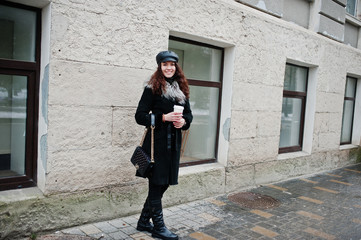 Fototapeta na wymiar Curly mexican girl in leather cap and plastic cup of coffee at hand walking at streets of city.