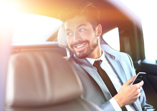 Unsmiling Businessman Sitting In The Back Seat In His Car