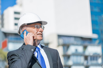 Man architector outdoor at construction area having mobile conversation