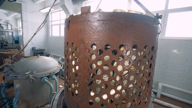 A pile of tin cans in a rusty container is being elevated from a boiler