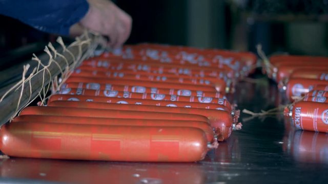 Sausage sticks are being tied up and hanged up by a factory worker