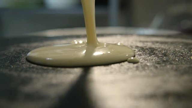 A wonderful view of a homemade pancake cooking. A female hand pours  liquid dough using a scoop. Then it spins pressing dough with a spoon 