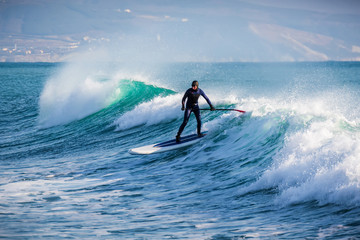 Surfer on stand up paddle board ride at wave. Winter surfing in ocean