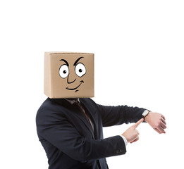 businessman with cardboard box on head pointing on wristwatch isolated on white