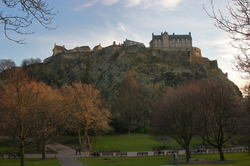 Skaliste wzgórze z zamkiem w Edynburgu, stolicy Szkocji, wczesna wiosna, u podnóża roślinność parku, bladobłękitne niebo