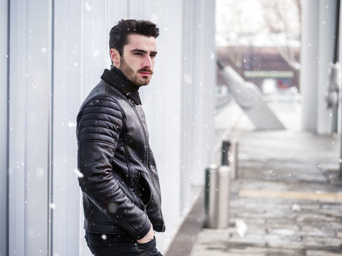 Handsome bearded young man outdoor in winter fashion, wearing black leather jacket in modern city setting